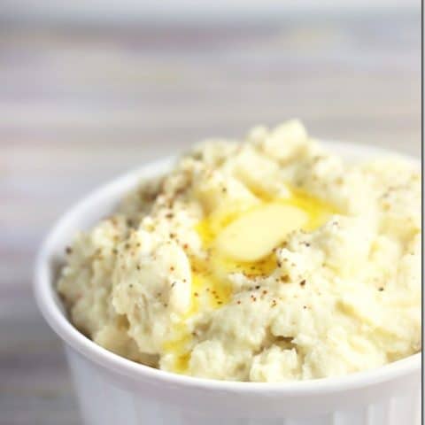 White bowl with mashed cauliflower and melted butter and pepper